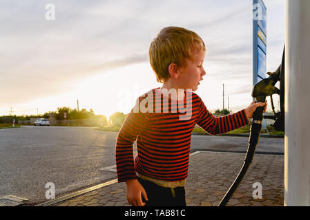 Bambino tenere il tubo di una pompa del carburante al tramonto in corrispondenza di una stazione di gas. Foto Stock