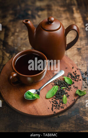 Il tè alla menta in marrone tazza di ceramica e teiera su un caldo sullo sfondo di legno con infuso di tè e foglie di menta. Foto Stock