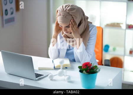 Avendo mal di testa. Scienziato medico indossa hijab avente mal di testa dopo una giornata di lavoro Foto Stock