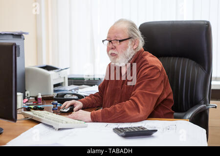 Concentrato senior barbuto uomo utilizzando computer presso la scrivania in ufficio, ingegnere collare bianco lavoratore, una persona Foto Stock