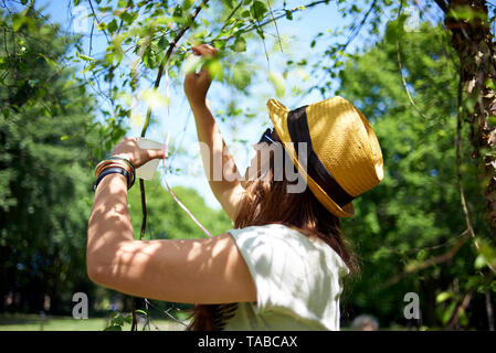 Felice close up di una Latina donna brasiliana che indossa un cappello di paglia al di fuori in un parco durante una festa di compleanno nel sole primaverile Foto Stock