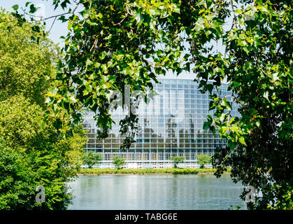 Ampia facciata del Parlamento europeo vista attraverso gli alberi della sede di Strasburgo un giorno prima del 2019 sulle elezioni per il Parlamento europeo - cielo blu chiaro e tranquillo fiume Ill acqua. Foto Stock