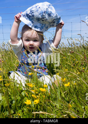 Baby girl giocando nel prato per un picnic estivo, tenendo il suo cappello Foto Stock