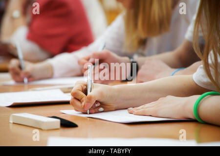 La ragazza scrive con una penna stilografica su un pezzo di carta durante le lezioni a scuola o all'università. Esame, esami. Senza un volto. Foto Stock