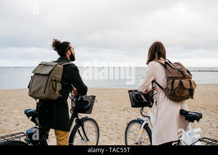 Coppia con e-bike sulla spiaggia guardando il mare Foto Stock