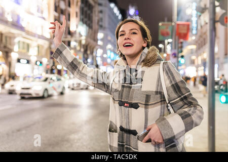 Spagna, Madrid, giovane donna nella città di notte accanto alla Gran Via salutando un taxi Foto Stock