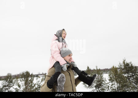 Padre che porta piccola figlia sulle sue spalle in inverno Foto Stock