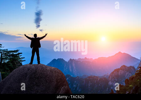 Escursionista è in piedi su una roccia con le mani alzate e godendo di sunrise Foto Stock