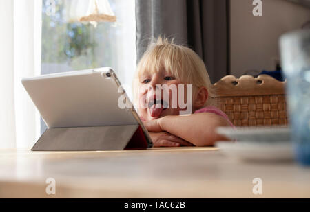 Ritratto di bionda bambina spuntavano lingua mentre guardano la tavoletta digitale Foto Stock