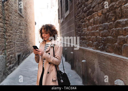 Donna in piedi in un vicolo tramite telefono cellulare Foto Stock