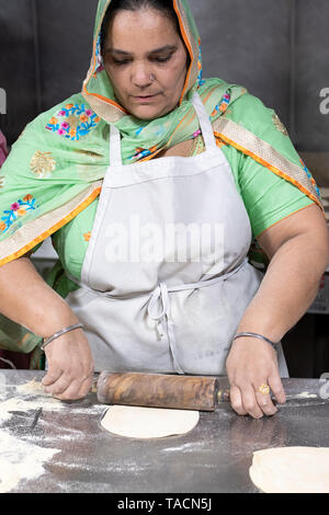 Una mezza età donna Sikh nei tradizionali vestiti etnici volontari e prepara il roti per essere servito nel tempio della langar (sala da pranzo). In Queens,NY Foto Stock