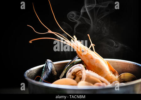 Molluschi piatto di frutti di mare con gamberi Calamari Cozze oceano cena gourmet a base di pesce bollito cotto in hot pot con erbe e spezie su backgroun scuro Foto Stock