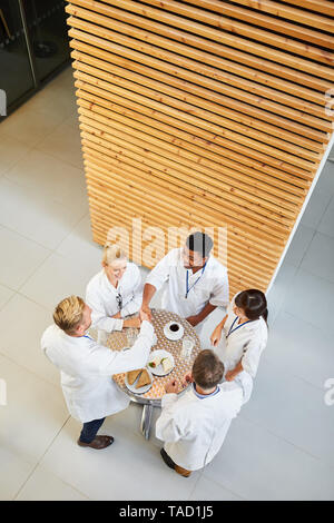 Il gruppo di medici nella caffetteria avente una pausa caffè mentre avente una piccola conversazione e mangiare Foto Stock