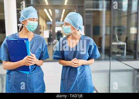 Due chirurghi in blu camici chirurgici e con maschere chirurgiche di fronte alla sala di emergenza Foto Stock