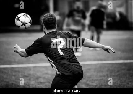 Roma, Italia - 19 Maggio 2019: giocatore di calcio in un campo di calcio insegue la palla in un gioco d'azione. Un Uomo in camicia nera e pantaloncini, incorniciato da dietro in Foto Stock