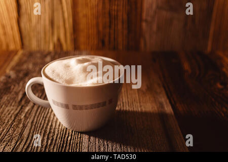 Caffè fresco guarnita con vegan latte di soia in una schiuma di colore bianco con coppa bruno rustico sfondo di legno in bella moody luce del sole di mattina Foto Stock