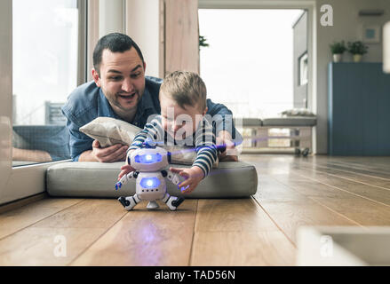 Entusiasta il padre e il figlio giacente su di un materasso a casa a giocare con un giocattolo robot Foto Stock