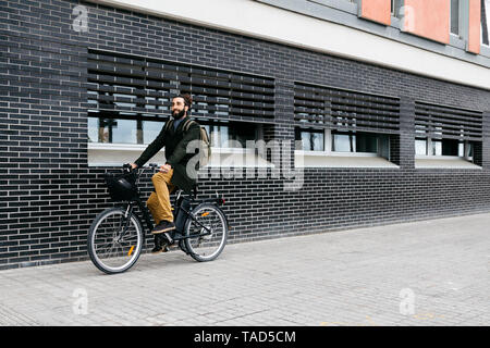 Uomo a cavallo e-bike lungo un muro di mattoni in città Foto Stock