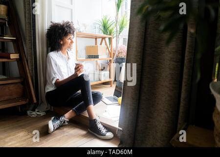 Rilassata donna seduta sul pavimento del suo appartamento, bere caffè Foto Stock
