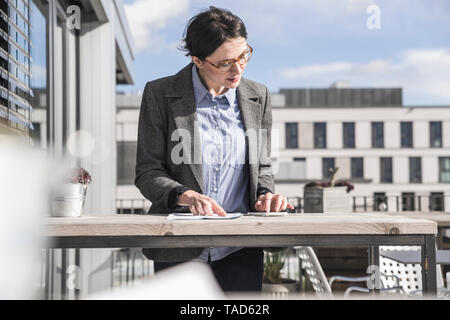 Imprenditrice tramite telefono cellulare sulla terrazza sul tetto Foto Stock