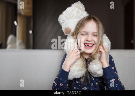 Ritratto di ridere bambina con dente divario azienda Orsacchiotto bianco Foto Stock