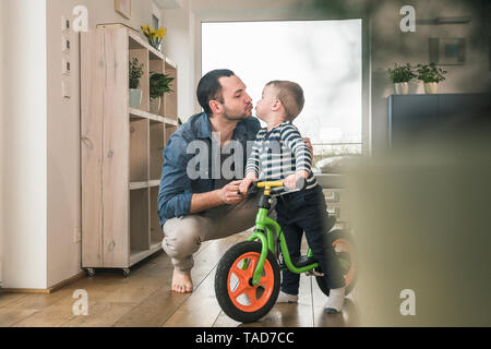 Padre baciare figlio con un equilibrio in bicicletta home Foto Stock