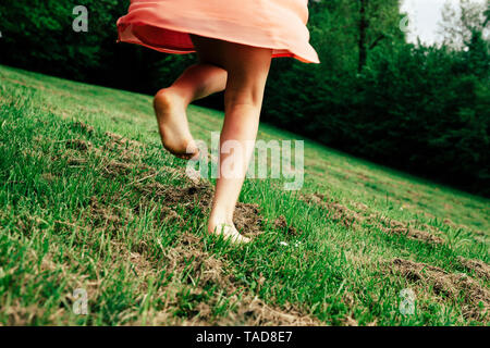 Vista posteriore di una ragazza correre a piedi nudi su un prato, vista parziale Foto Stock