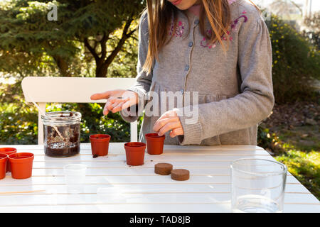 Bambina al tavolo da giardino la semina di semi, vista parziale Foto Stock