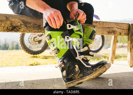 Motocross guidatore seduto su una panchina mettendo su indumenti di protezione Foto Stock