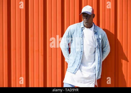 Uomo che indossa casual abbigliamento denim e cappuccio in piedi nella parte anteriore della parete arancione Foto Stock