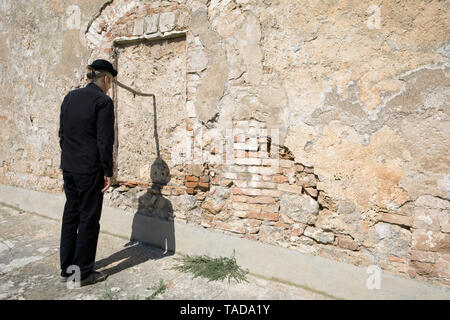 Uomo che indossa un cappello bowler equilibratura di un bastone a un muro di pietra Foto Stock