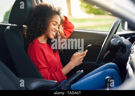 Sorridente giovane donna utilizzando il cellulare in una macchina Foto Stock