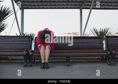 Premuto donna con capelli ricci seduta su una panchina Foto Stock