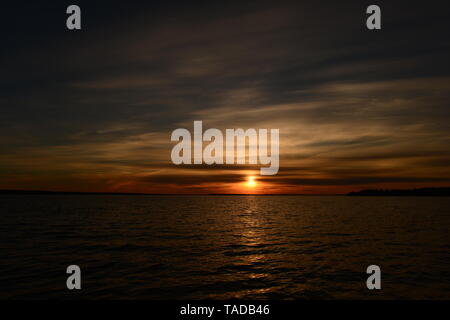 Tramonto cerchio di Sun in grado di nebulosità di un cielo nuvoloso al di sopra della superficie dell'acqua del lago Foto Stock