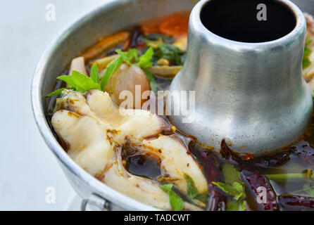 Piccante e speziato di una zuppa di pesce / Tilapia pesce cucinato con erbe aromatiche e spezie in hot pot sul tavolo da pranzo in stile tailandese cibo Foto Stock