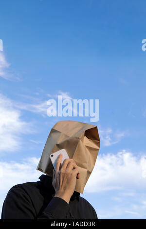 Uomo con sacchetto di carta sopra la sua testa parlando al cellulare Foto Stock