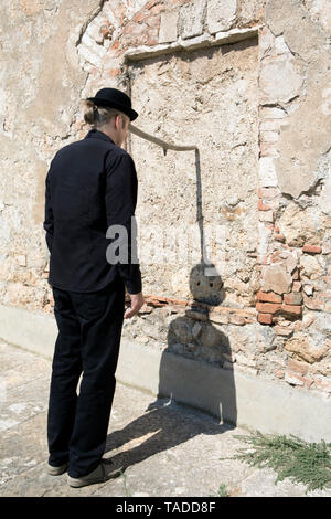 Uomo che indossa un cappello bowler equilibratura di un bastone a un muro di pietra Foto Stock