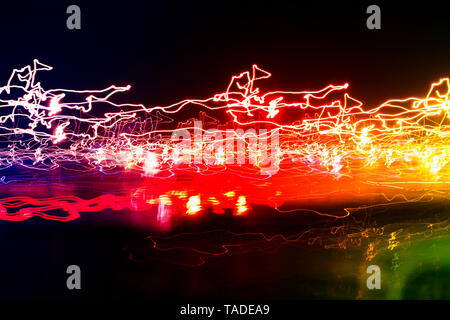 Diversi sentieri di luce di variopinte lanterne di strada e macchine passando la dispersione nel buio, una lunga esposizione urbana sfondo astratto Foto Stock