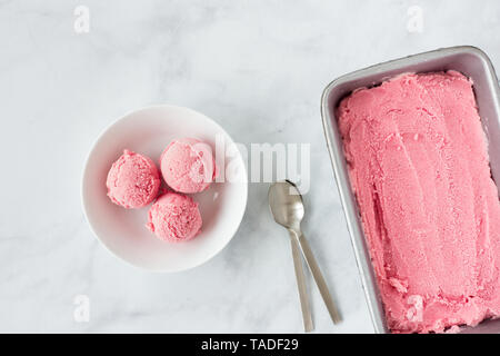 Rosa costretto rabarbaro gelato nel contenitore e ciotola con cucchiai su marmo bianco sfondo con copia spazio. Vista dall'alto. Foto Stock