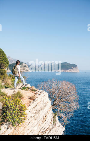 Un turista con lo zaino sulla cima di una scogliera o collina vicino al mare appare in lontananza. Viaggiare da soli. Foto Stock