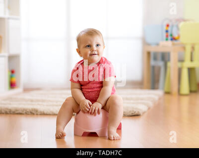 Poco sorridente bambina seduta su una pentola. Isolato su sfondo bianco. Foto Stock