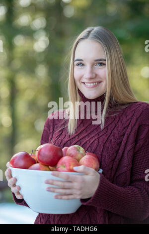 Ritratto di sorridente ragazza bionda azienda ciotola di mele Foto Stock