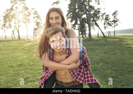 Ritratto di felice giovane ragazza portante piggyback su prato Foto Stock