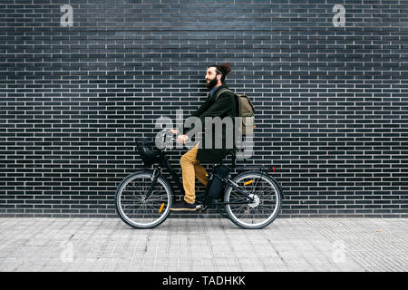 Uomo a cavallo e-bike lungo una parete di mattoni Foto Stock