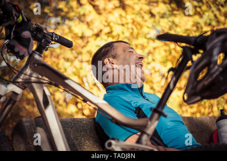 Laughing Man con mountainbike avente una pausa seduta su una panchina Foto Stock