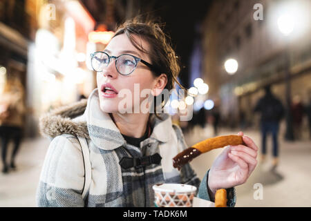 Spagna, Madrid, giovane donna nella città di notte mangiare tipico churros con il cioccolato Foto Stock