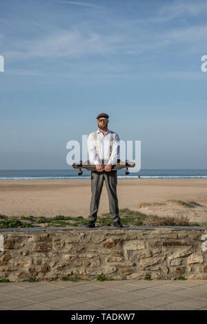 Uomo con longboard in piedi su una parete di fronte spiaggia e mare Foto Stock