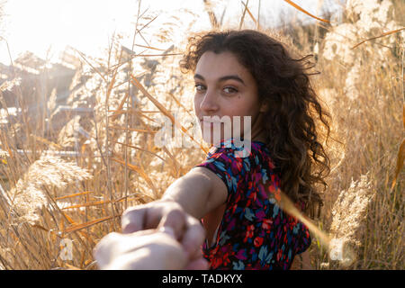 Giovane donna in piedi nel prato, tenendo la mano di un uomo giovane Foto Stock
