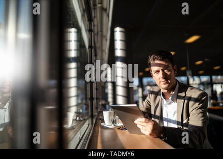 Ritratto di imprenditore utilizzando compressa alla finestra in un cafe Foto Stock