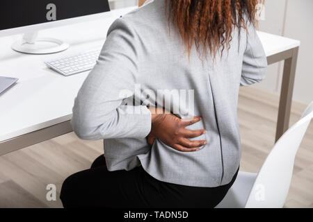Vista laterale di African imprenditrice tenendo la schiena mentre si lavora sul computer portatile alla scrivania in ufficio Foto Stock